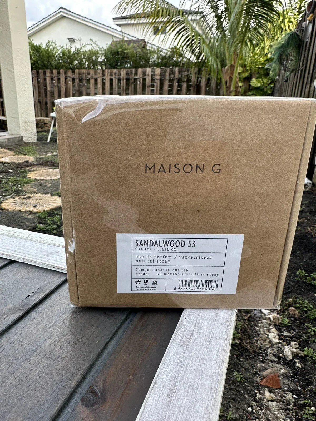 Cardboard box with 'Maison G' branding on a wooden surface outdoors.